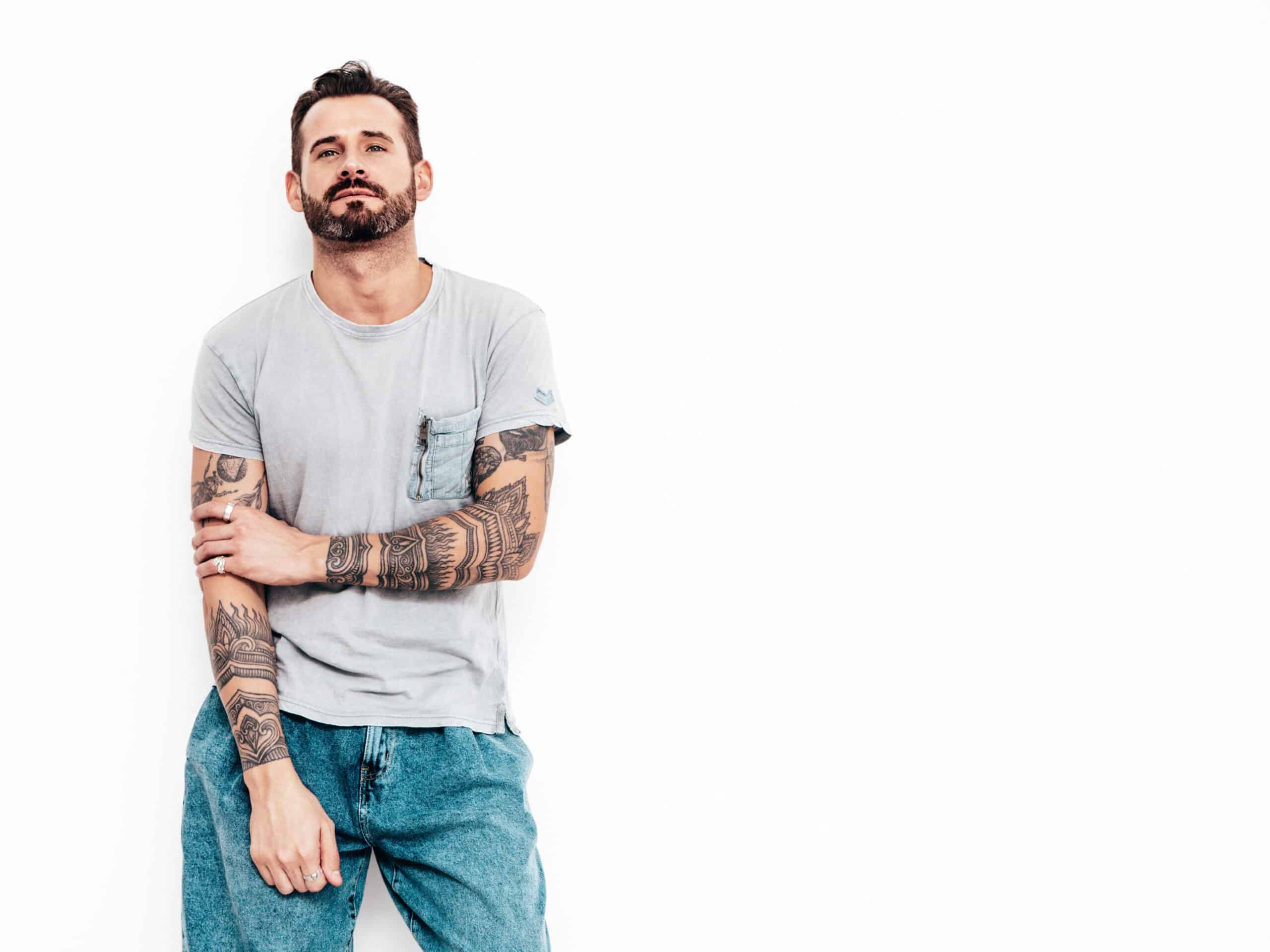Portrait of handsome confident stylish hipster lambersexual model. Sexy man dressed in T-shirt and jeans. Fashion male isolated on white wall in studio